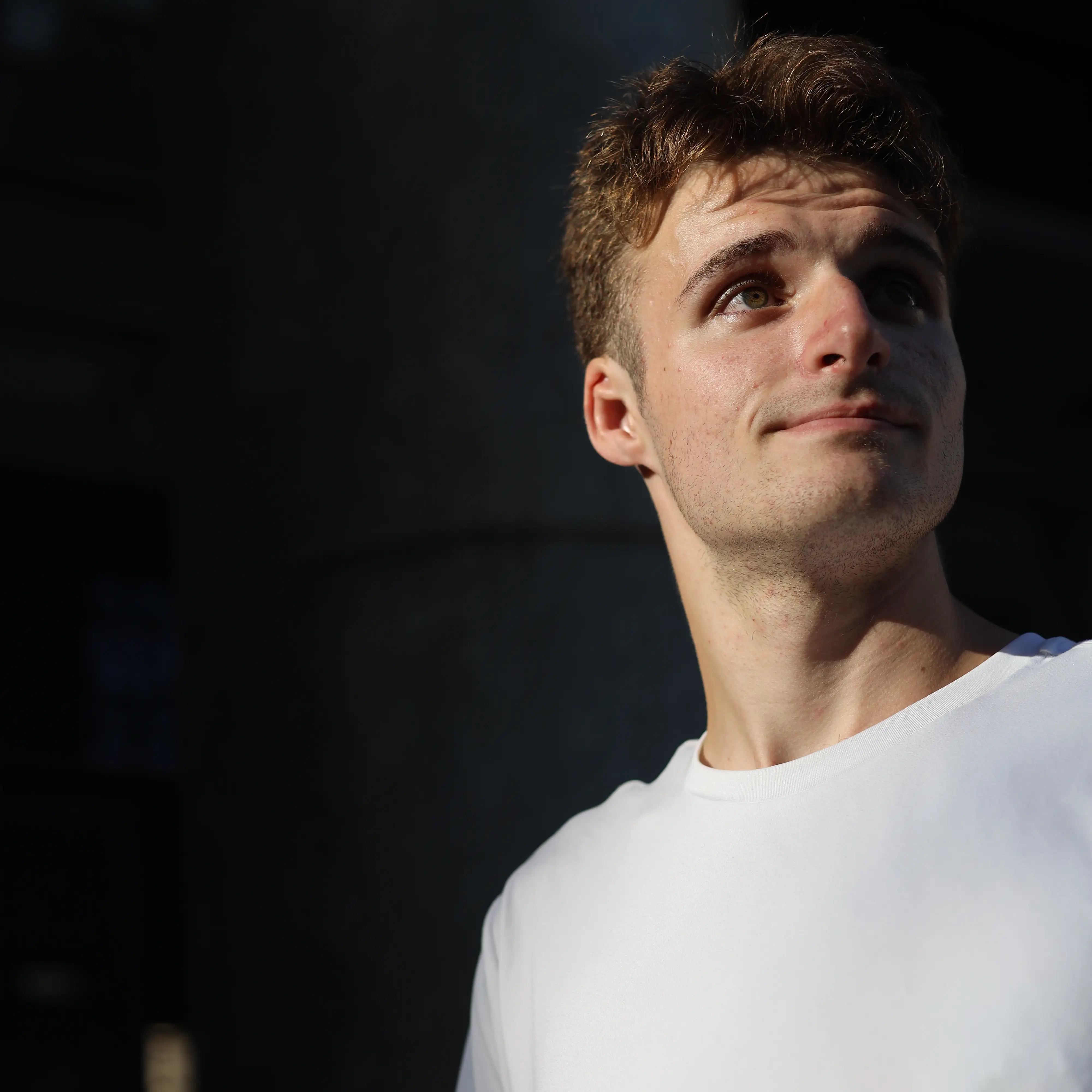 Close-up portrait of a young man in a white t-shirt looking up