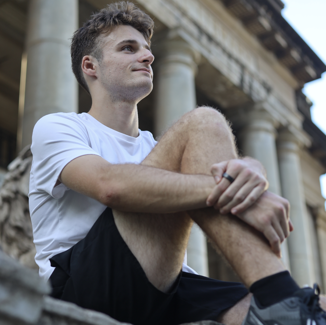 Lifestyle portrait of a young man sitting on steps in front of a classic building